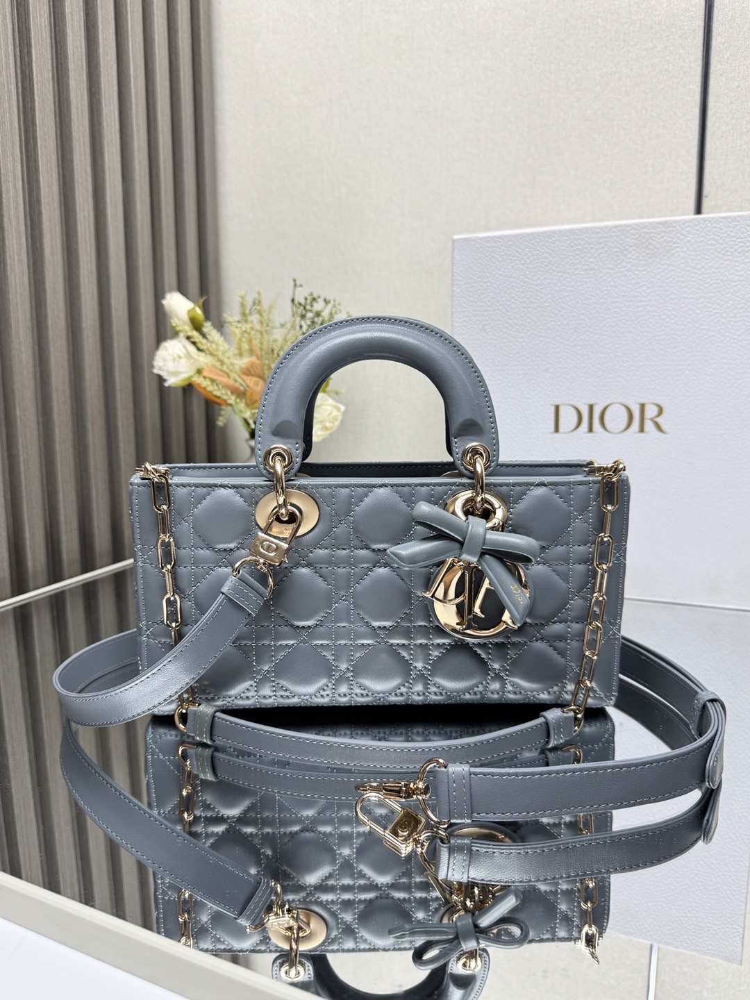 中号 LADY D-JOY 手袋 雾霾蓝带蝴蝶结小羊皮 这款 Lady D-Joy 手袋凸显 Lady Dior 系列的简约美学 集中体现了 Dior 对典雅和美丽的深刻洞见 采用黑色哑光牛皮革精心制作 以经典的藤格纹缉面线打造醒目的绗缝细节 精良的缝制工艺显露无遗 同色调金属 D.I.O.R. 吊饰彰显优雅气质 小号款式 搭配可拆卸的链条肩带和可调节 可拆卸的皮革肩带 可手提 肩背或斜挎 是日常造型的理想之选 可拆卸链条肩带可拆卸 可调节的皮革肩带型号 0540尺寸 26×13.5×5 cm可收纳一部 iPhone和其他配饰238620
