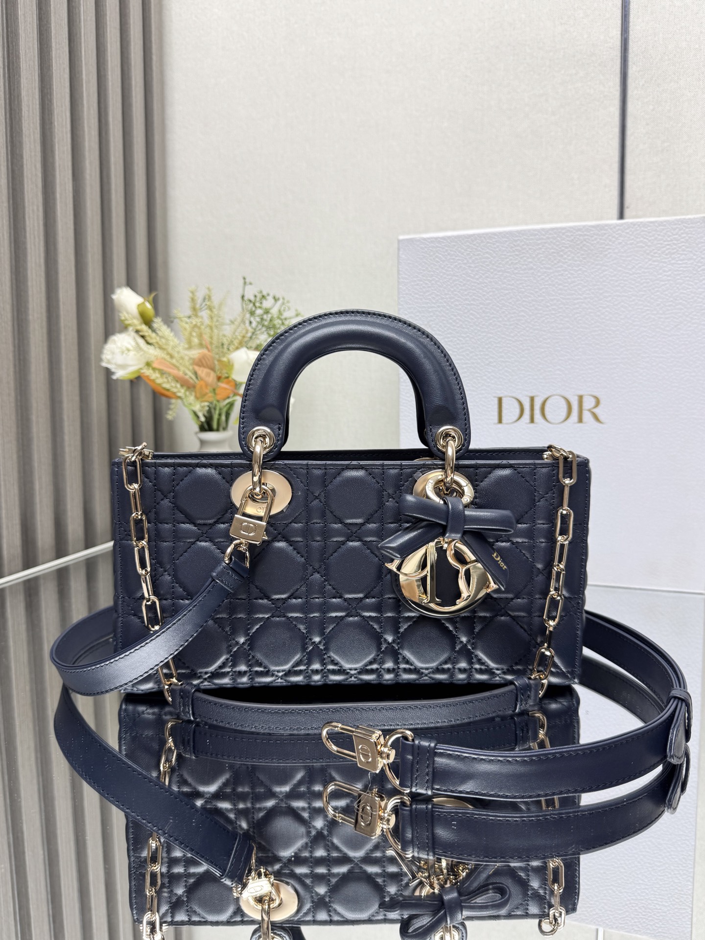 中号 LADY D-JOY 手袋 深蓝色带蝴蝶结小羊皮 这款 Lady D-Joy 手袋凸显 Lady Dior 系列的简约美学 集中体现了 Dior 对典雅和美丽的深刻洞见 采用黑色哑光牛皮革精心制作 以经典的藤格纹缉面线打造醒目的绗缝细节 精良的缝制工艺显露无遗 同色调金属 D.I.O.R. 吊饰彰显优雅气质 小号款式 搭配可拆卸的链条肩带和可调节 可拆卸的皮革肩带 可手提 肩背或斜挎 是日常造型的理想之选 可拆卸链条肩带可拆卸 可调节的皮革肩带型号 0540尺寸 26×13.5×5 cm可收纳一部 iPhone和其他配饰238620