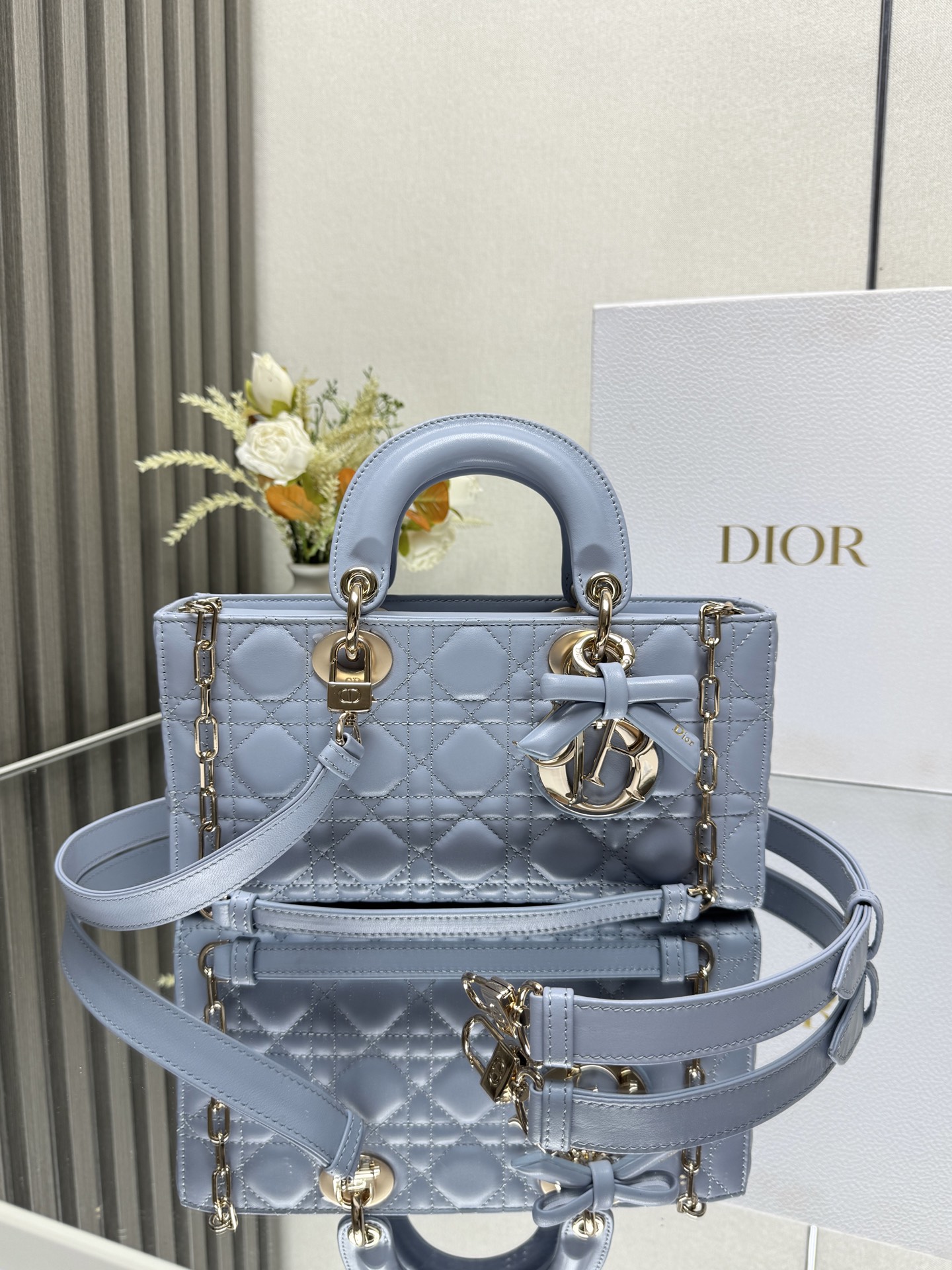中号 LADY D-JOY 手袋 淡蓝色带蝴蝶结小羊皮 这款 Lady D-Joy 手袋凸显 Lady Dior 系列的简约美学 集中体现了 Dior 对典雅和美丽的深刻洞见 采用黑色哑光牛皮革精心制作 以经典的藤格纹缉面线打造醒目的绗缝细节 精良的缝制工艺显露无遗 同色调金属 D.I.O.R. 吊饰彰显优雅气质 小号款式 搭配可拆卸的链条肩带和可调节 可拆卸的皮革肩带 可手提 肩背或斜挎 是日常造型的理想之选 可拆卸链条肩带可拆卸 可调节的皮革肩带型号 0540尺寸 26×13.5×5 cm可收纳一部 iPhone和其他配饰238620