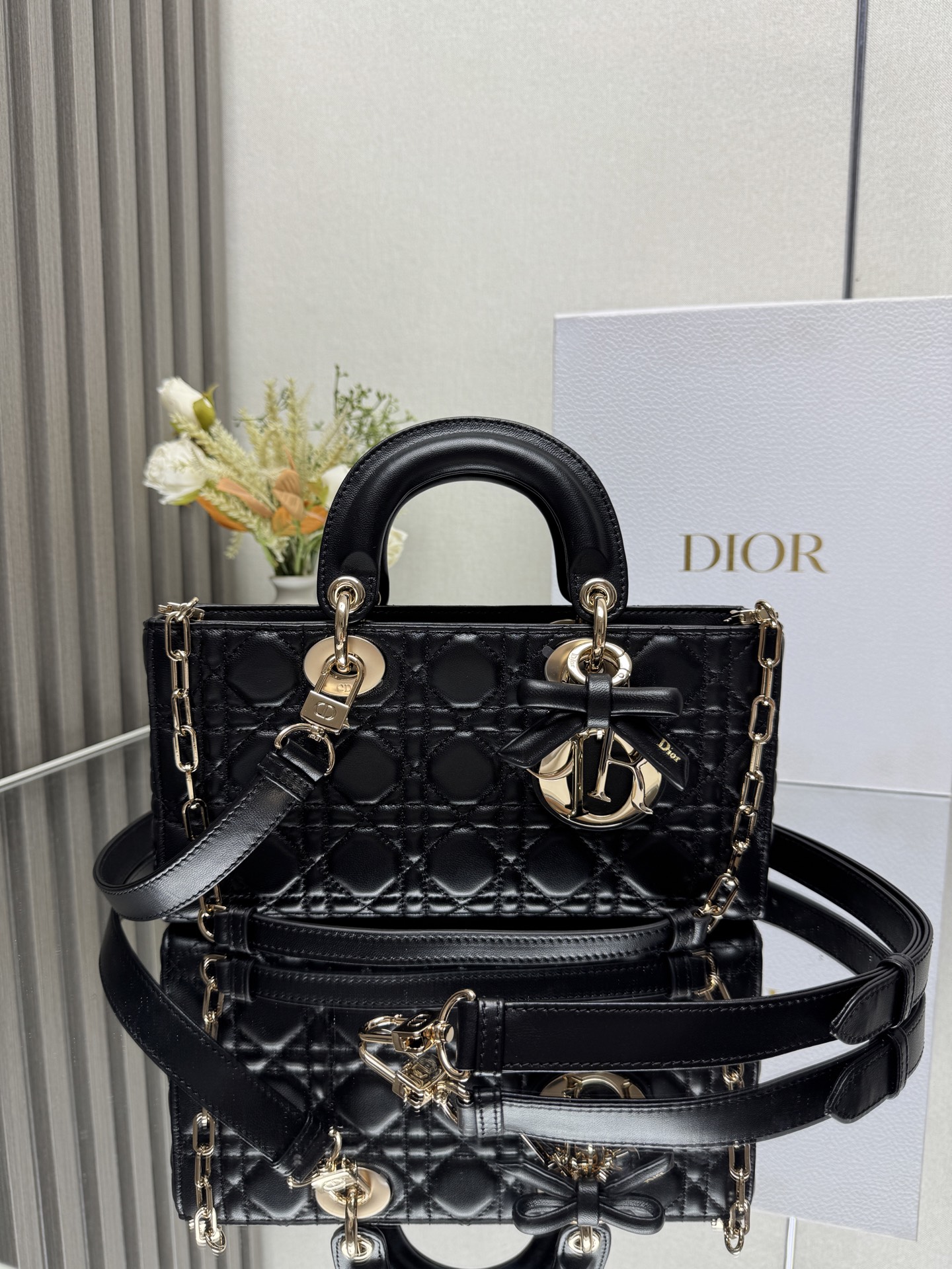 中号 LADY D-JOY 手袋 黑色带蝴蝶结小羊皮 这款 Lady D-Joy 手袋凸显 Lady Dior 系列的简约美学 集中体现了 Dior 对典雅和美丽的深刻洞见 采用黑色哑光牛皮革精心制作 以经典的藤格纹缉面线打造醒目的绗缝细节 精良的缝制工艺显露无遗 同色调金属 D.I.O.R. 吊饰彰显优雅气质 小号款式 搭配可拆卸的链条肩带和可调节 可拆卸的皮革肩带 可手提 肩背或斜挎 是日常造型的理想之选 可拆卸链条肩带可拆卸 可调节的皮革肩带型号 0540尺寸 26×13.5×5 cm可收纳一部 iPhone和其他配饰238620