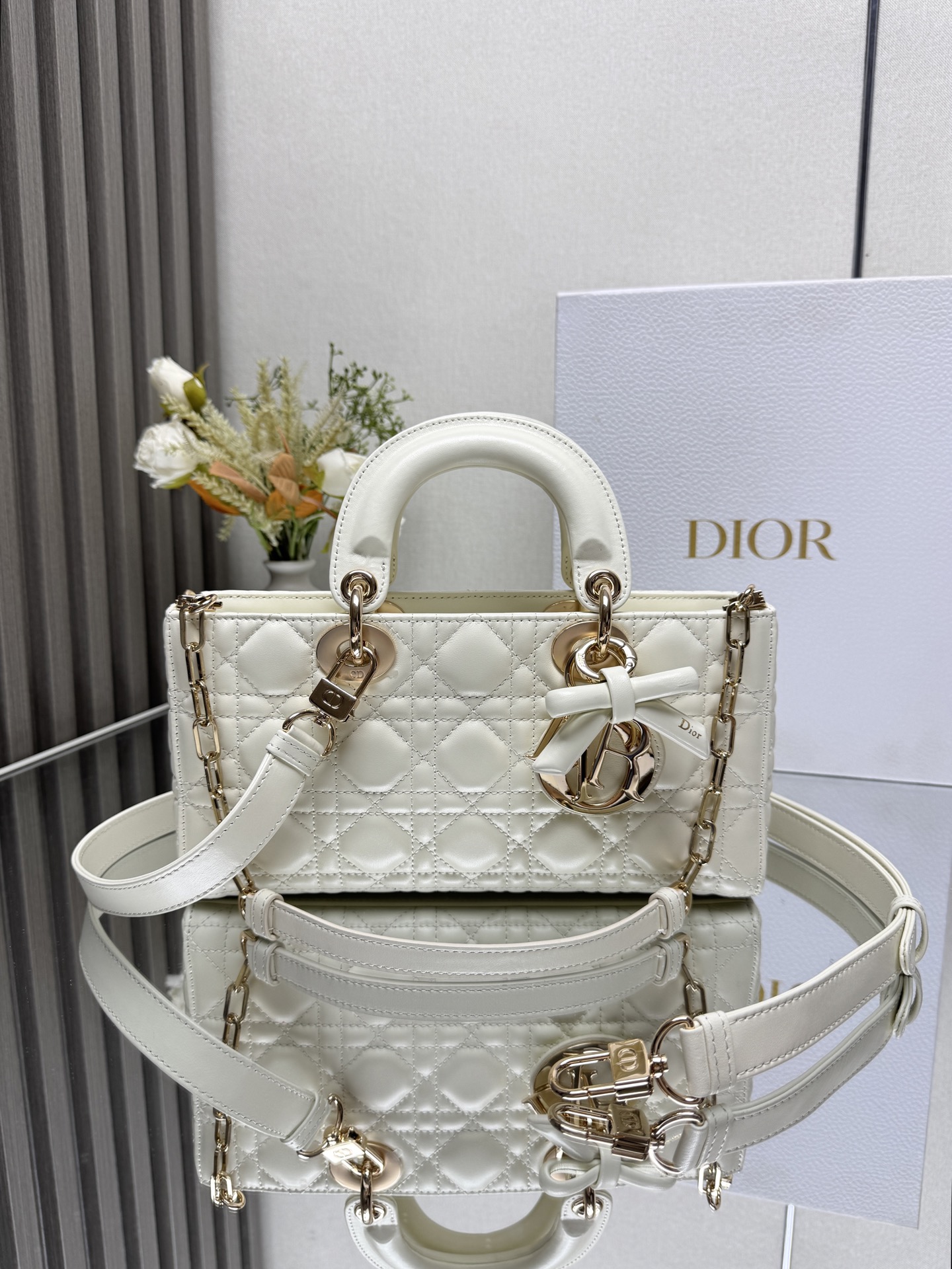 中号 LADY D-JOY 手袋 白色带蝴蝶结小羊皮 这款 Lady D-Joy 手袋凸显 Lady Dior 系列的简约美学 集中体现了 Dior 对典雅和美丽的深刻洞见 采用黑色哑光牛皮革精心制作 以经典的藤格纹缉面线打造醒目的绗缝细节 精良的缝制工艺显露无遗 同色调金属 D.I.O.R. 吊饰彰显优雅气质 小号款式 搭配可拆卸的链条肩带和可调节 可拆卸的皮革肩带 可手提 肩背或斜挎 是日常造型的理想之选 可拆卸链条肩带可拆卸 可调节的皮革肩带型号 0540尺寸 26×13.5×5 cm可收纳一部 iPhone和其他配饰238620